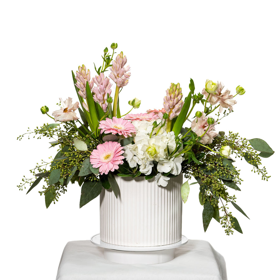 Trendy arrangement of pink gerberas, hyacinth and mixed blooms in a white fluted pot