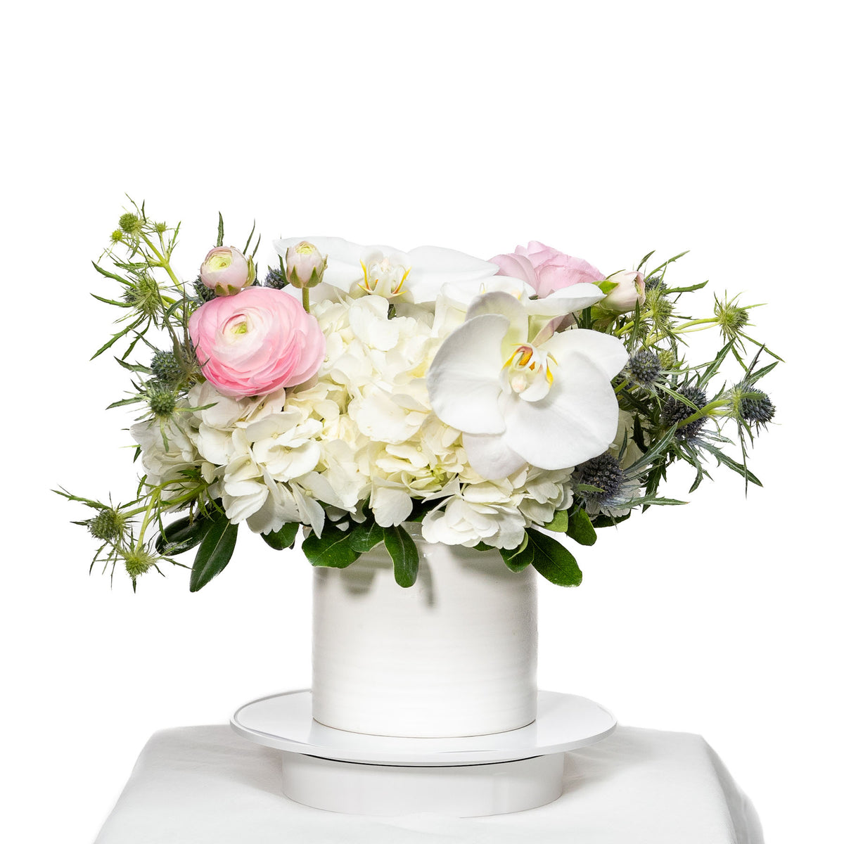 Romantica arrangement of white orchids, hydrangea and blush ranunculus in a white pot
