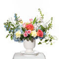 Radiance arrangement of blue delphinium, peach roses and white stock in a white footed urn