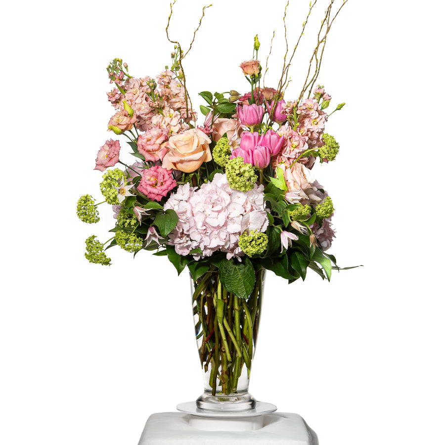 Pristine arrangement of blush roses, lisianthus and viburnum in a tall glass vase