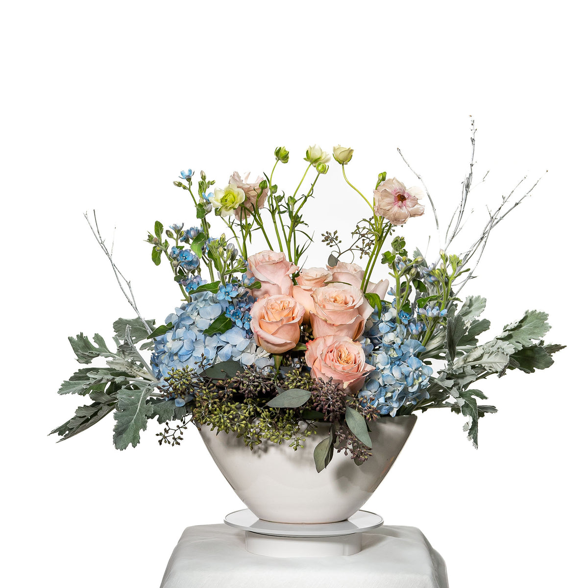 Morning Breeze arrangement of blue hydrangea, peach roses and dusty miller in a silver bowl