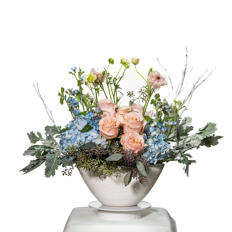 Morning Breeze arrangement of blue hydrangea, peach roses and dusty miller in a silver bowl