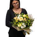 Harmony bouquet of cream roses, yellow blooms and greenery, held by a florist