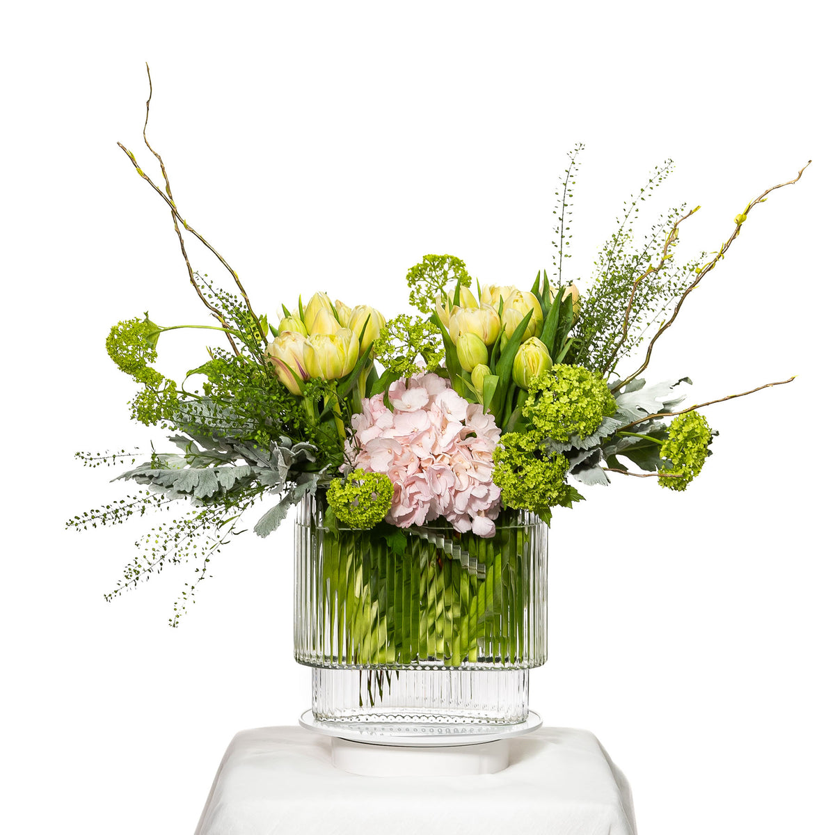 Fleurish arrangement of green hydrangea, cream tulips and willow in a ribbed glass vase