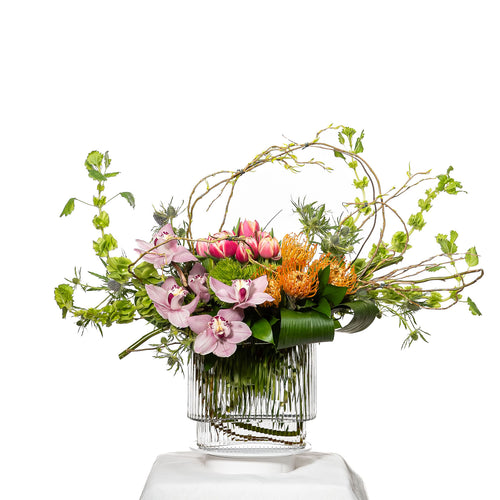 Delighted arrangement of pink and orange roses with trailing greenery in a ribbed glass vase