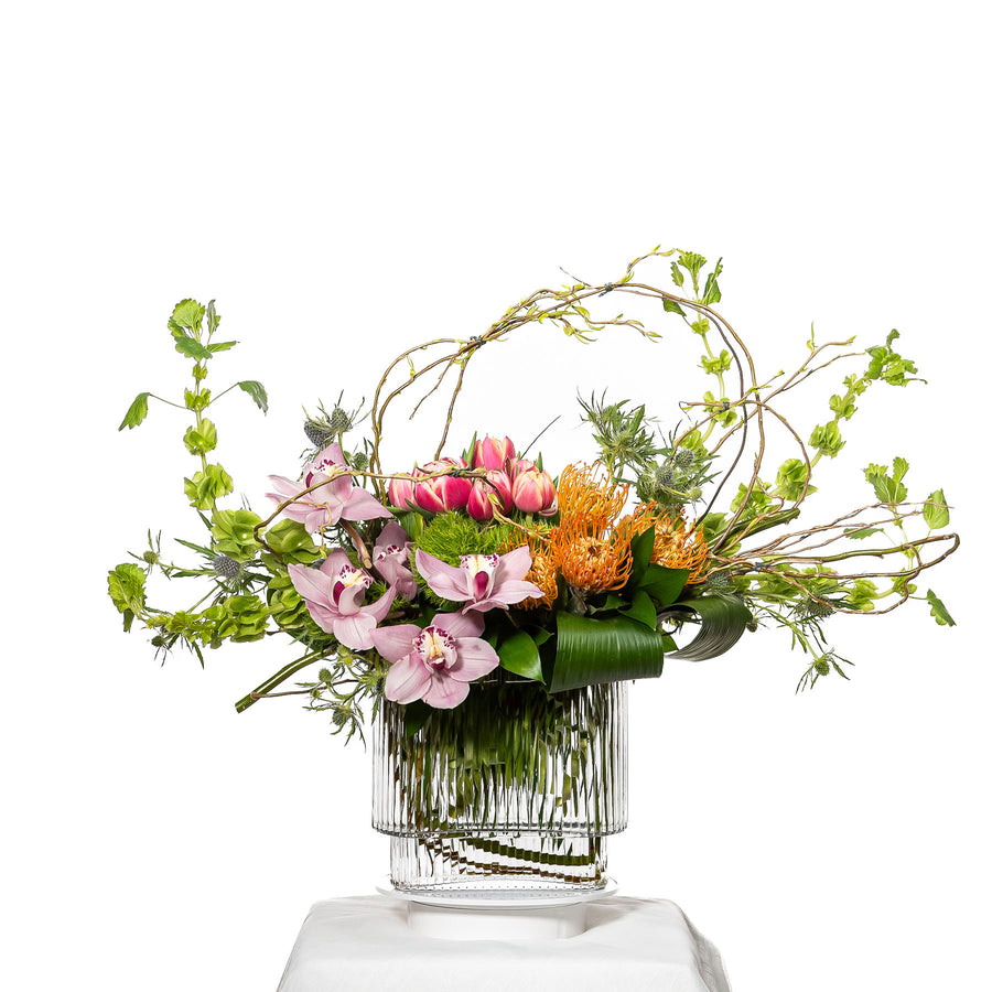 Delighted arrangement of pink and orange roses with trailing greenery in a ribbed glass vase