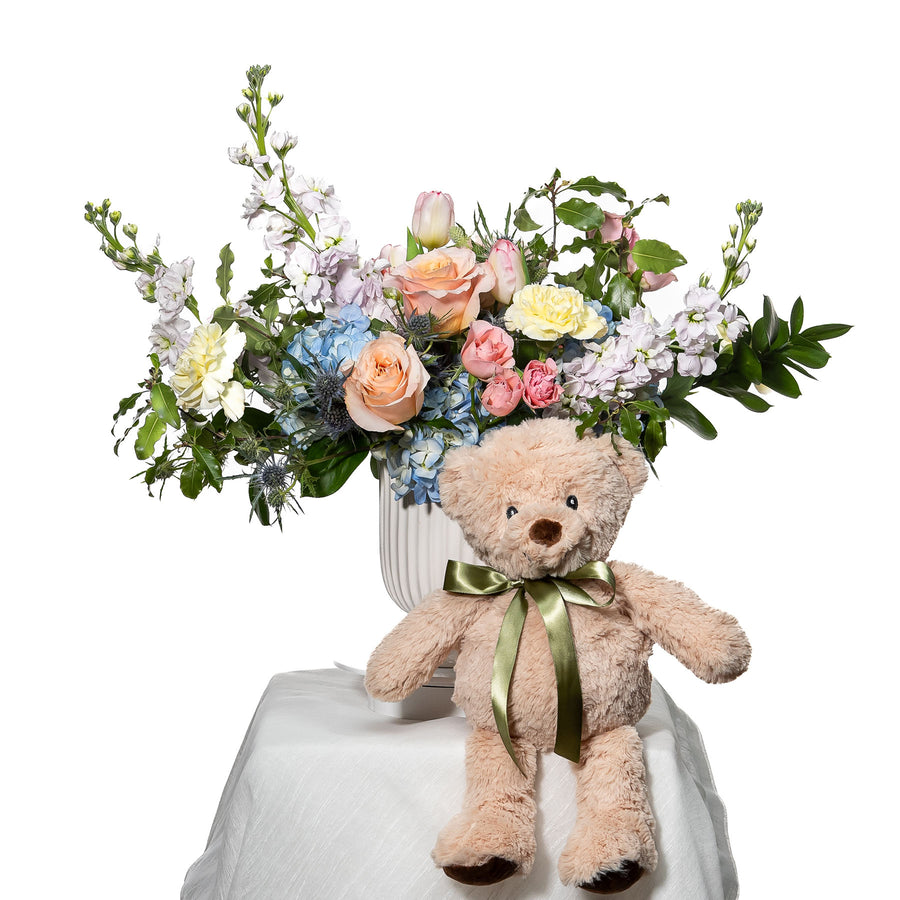 Bundle of Joy arrangement of pastel roses and delphinium with a plush teddy bear at the base