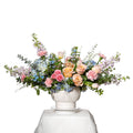 Buds in Bloom arrangement of blue delphinium, peach roses and pink stock in a white fluted pot