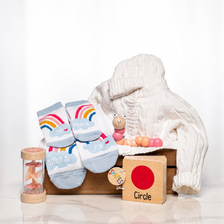 Classic Comforts baby girl gift with a cream knitted set, rainbow socks, a rattle and wooden toys