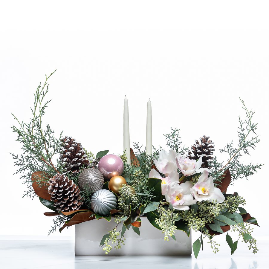 Blush and Balsam Beauty arrangement with white candles, pastel baubles, orchids and pine cones