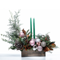 Blush and Balsam Glow arrangement with green taper candles, pink baubles and pine cones in a wooden box