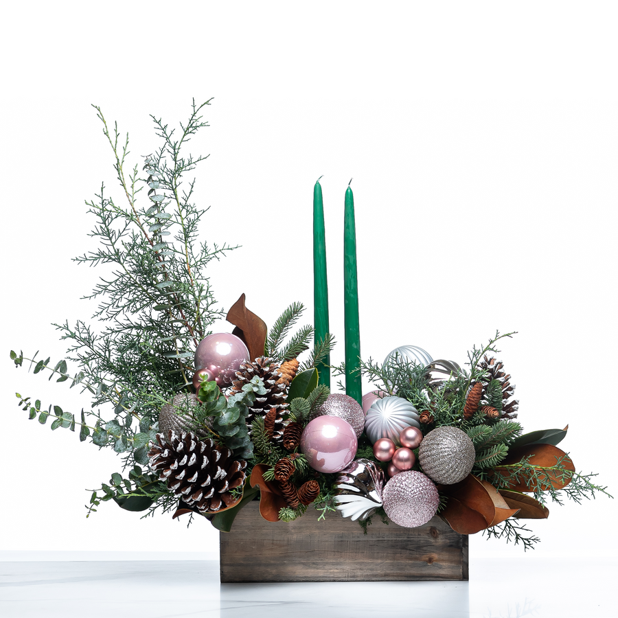Blush and Balsam Glow arrangement with green taper candles, pink baubles and pine cones in a wooden box