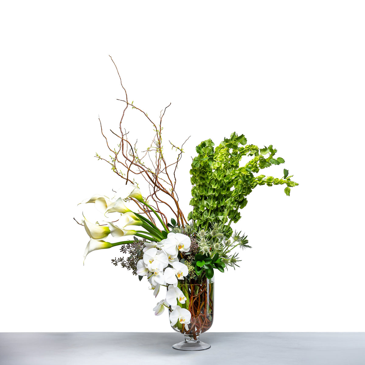 Botanical Rise arrangement of white calla lilies, orchids and greenery in a glass vase