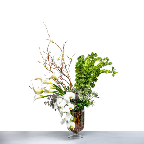 Botanical Rise arrangement of white calla lilies, orchids and greenery in a glass vase