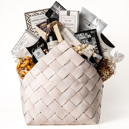 Bountiful Bundle Large: a white washed woven carrier with a bottle of red wine, Castello brie, grissini, crackers, cookie crisps, biscotti and gourmet snacks