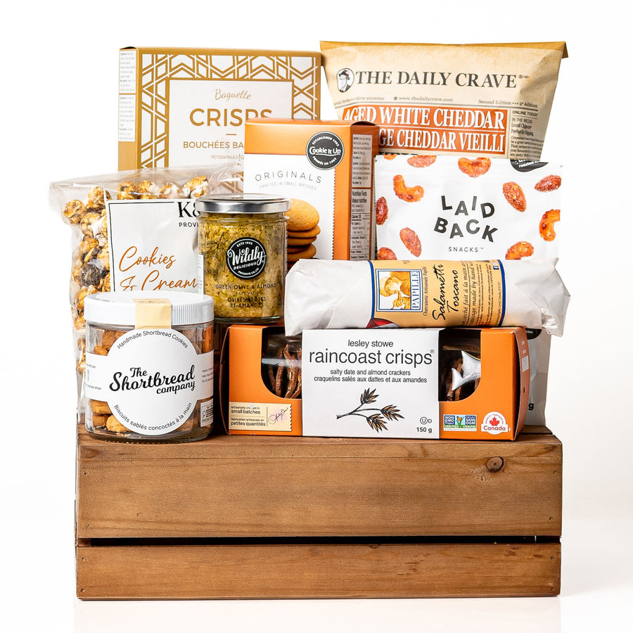 Canadian Cravings: a brown slotted wood crate with a jar of shortbread cookies, Raincoast Crisps, Laid Back snack mix, lentil chips, olive tapenade and caramel popcorn