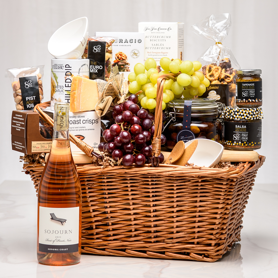 Charcuterie gift basket in a wicker hamper with cheese, crackers, grapes, preserves and a bottle of rose wine