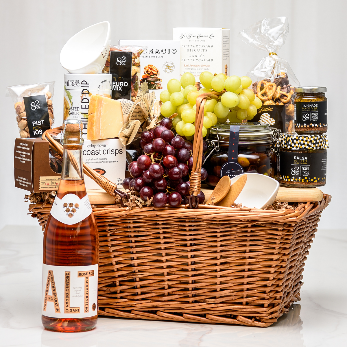 Charcuterie gift basket in a wicker hamper with cheese, crackers, grapes, preserves and non-alcoholic rose