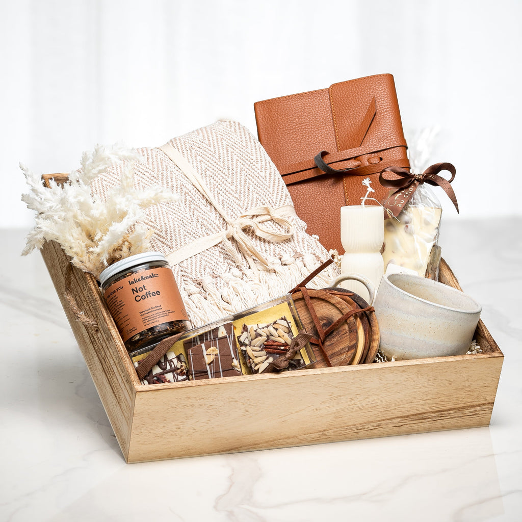 Chestnut gift tray with a knitted throw, a leather journal, a candle and a ceramic cup