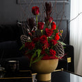 Crimson arrangement of red roses with pine, berries and blossom branches in a gold footed bowl