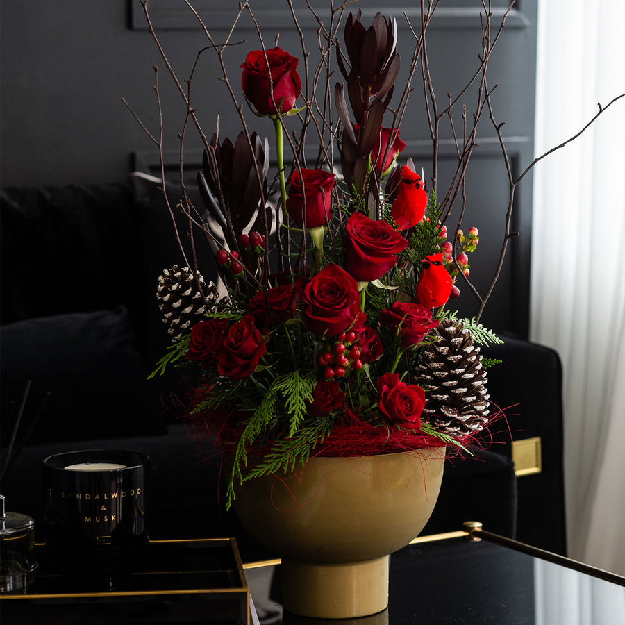 Crimson arrangement of red roses with pine, berries and blossom branches in a gold footed bowl