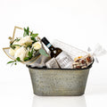 Elegance Small gift basket: a galvanised oval tub with a bouquet of white roses, a bottle of red wine, cashew roca, Desobry biscuits and white chocolate crunch bark