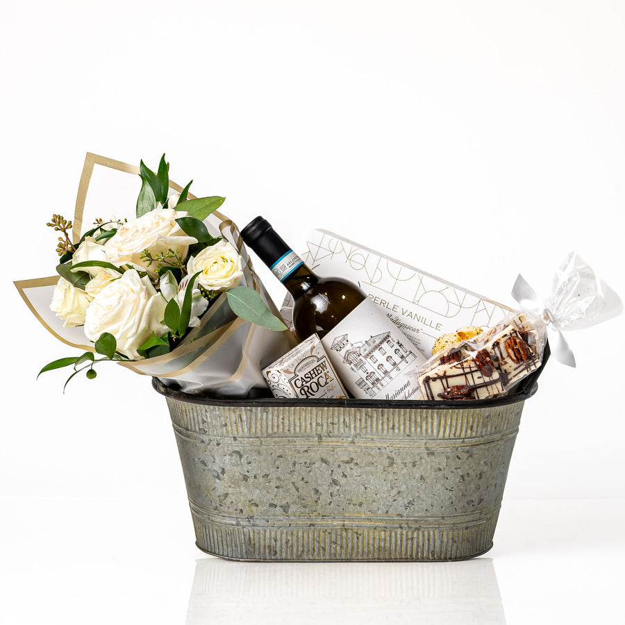 Elegance Small gift basket: a galvanised oval tub with a bouquet of white roses, a bottle of red wine, cashew roca, Desobry biscuits and white chocolate crunch bark