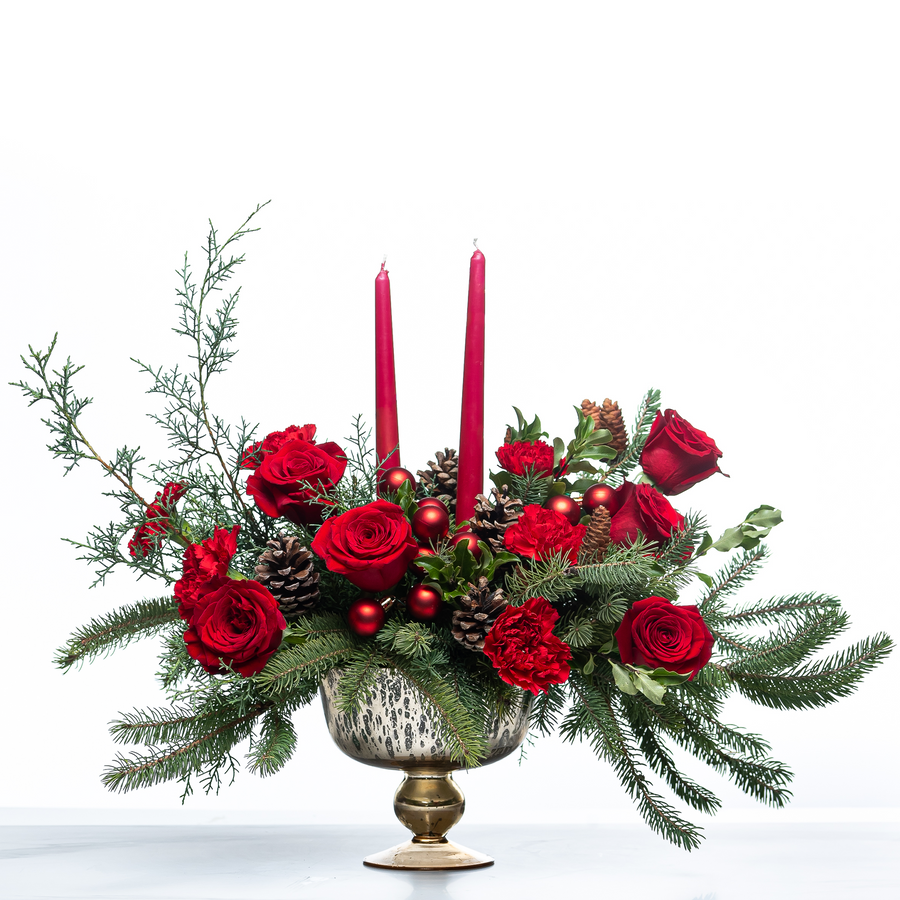 Festive Ruby Glow arrangement of red roses with red taper candles and pine in a gold footed bowl