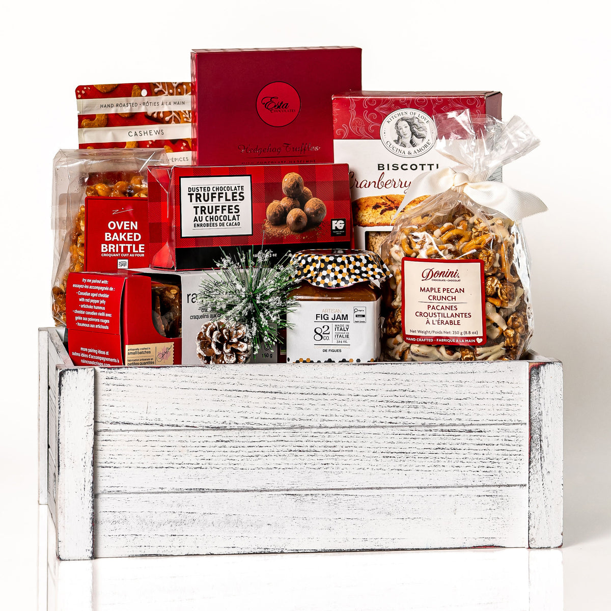 Festive Faves Large: a white washed slotted wood crate with dusted chocolate truffles, oven baked brittle, biscotti, fig jam, maple pecan popcorn and gingerbread cashews, finished with a pinecone