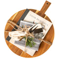 From the Kitchen gift: a round acacia wood serving board with the Cook Beautiful cookbook, three cheese knives with gold handles and a cotton kitchen towel tied with twine