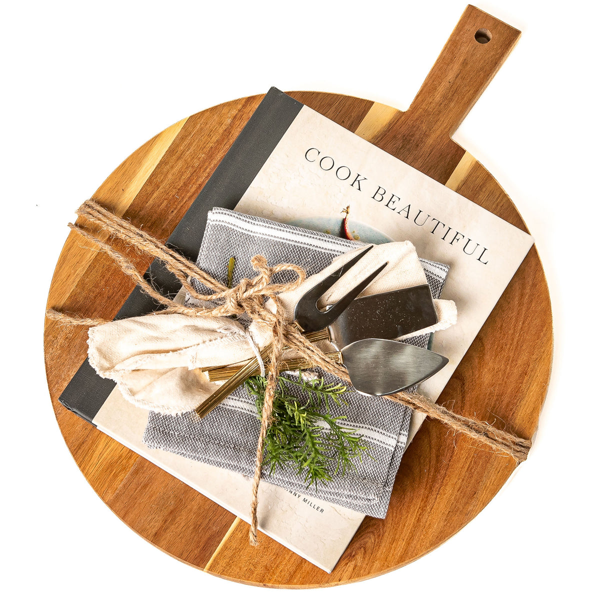 From the Kitchen gift: a round acacia wood serving board with the Cook Beautiful cookbook, three cheese knives with gold handles and a cotton kitchen towel tied with twine