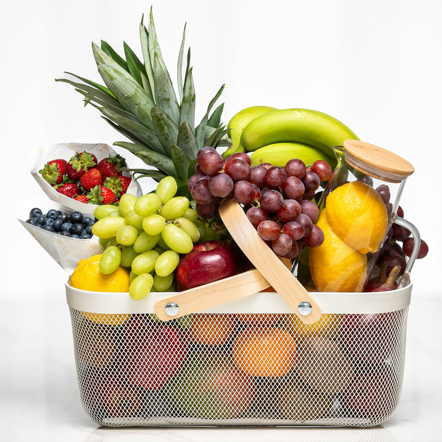 Large fresh fruit basket with pineapple, grapes, apples, bananas, berries and citrus in a wire basket