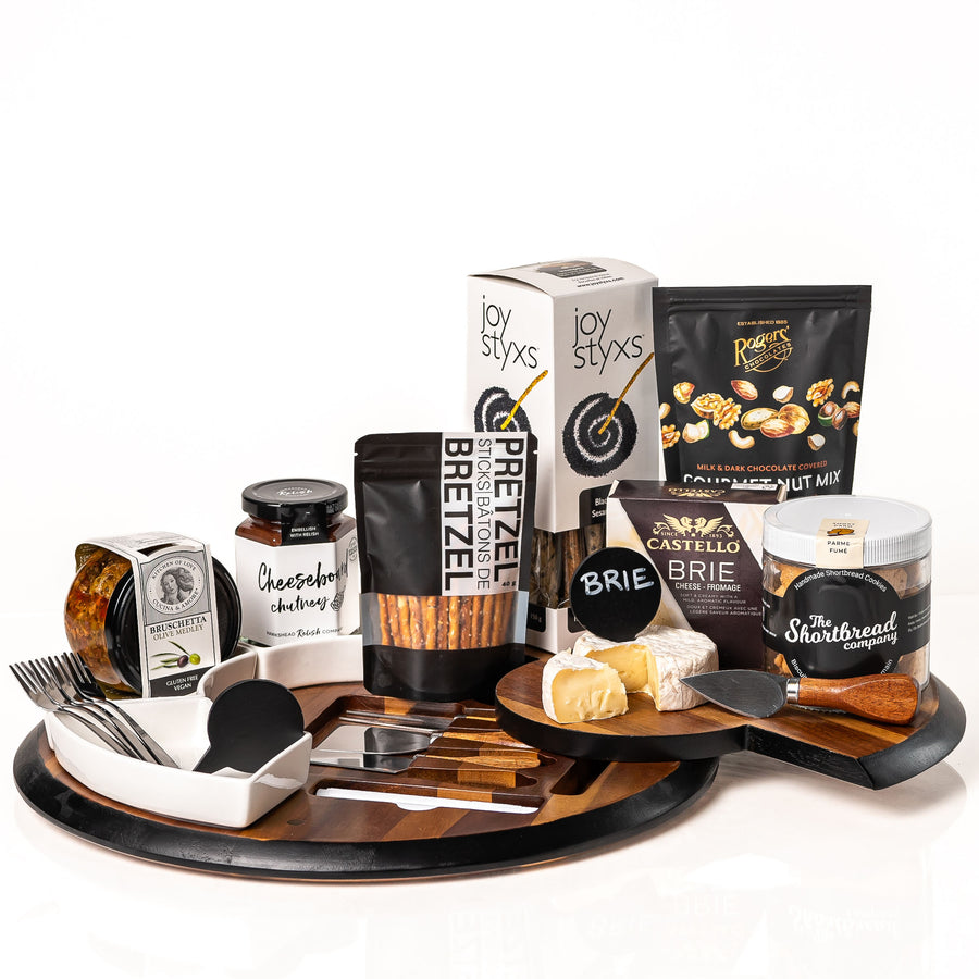 Gather & Graze gift: a round acacia serving board with ceramic dishes, cheese knives, forks and a chalkboard sign, with Castello brie, cheeseboard chutney, bruschetta, Joystyx and shortbread
