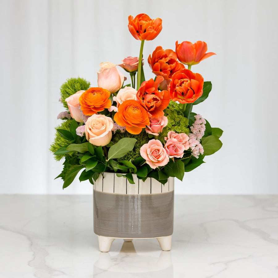 Golden Hour arrangement of orange tulips, roses and ranunculus in a two tone ceramic pot