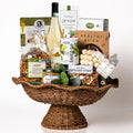 Heirloom Harvest: a wicker pedestal bowl with a wavy rim holding a bottle of Fonteamonte Trebbiano, a baked spinach dip, Raincoast Crisps, grissini, yogurt covered blueberries and biscotti