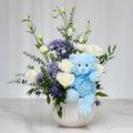 It's a Boy arrangement of white roses and blue blooms with a blue teddy bear in a white vase