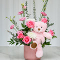 It's a Girl arrangement of pink roses and greenery with a pink teddy bear in a pink ceramic vase