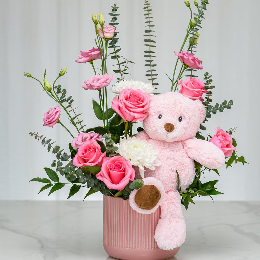 It's a Girl arrangement of pink roses and greenery with a pink teddy bear in a pink ceramic vase