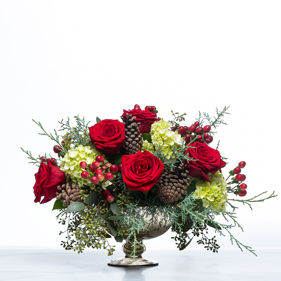 Merry and Bright centrepiece of red roses, green hydrangea, pine cones and berries in a footed bowl