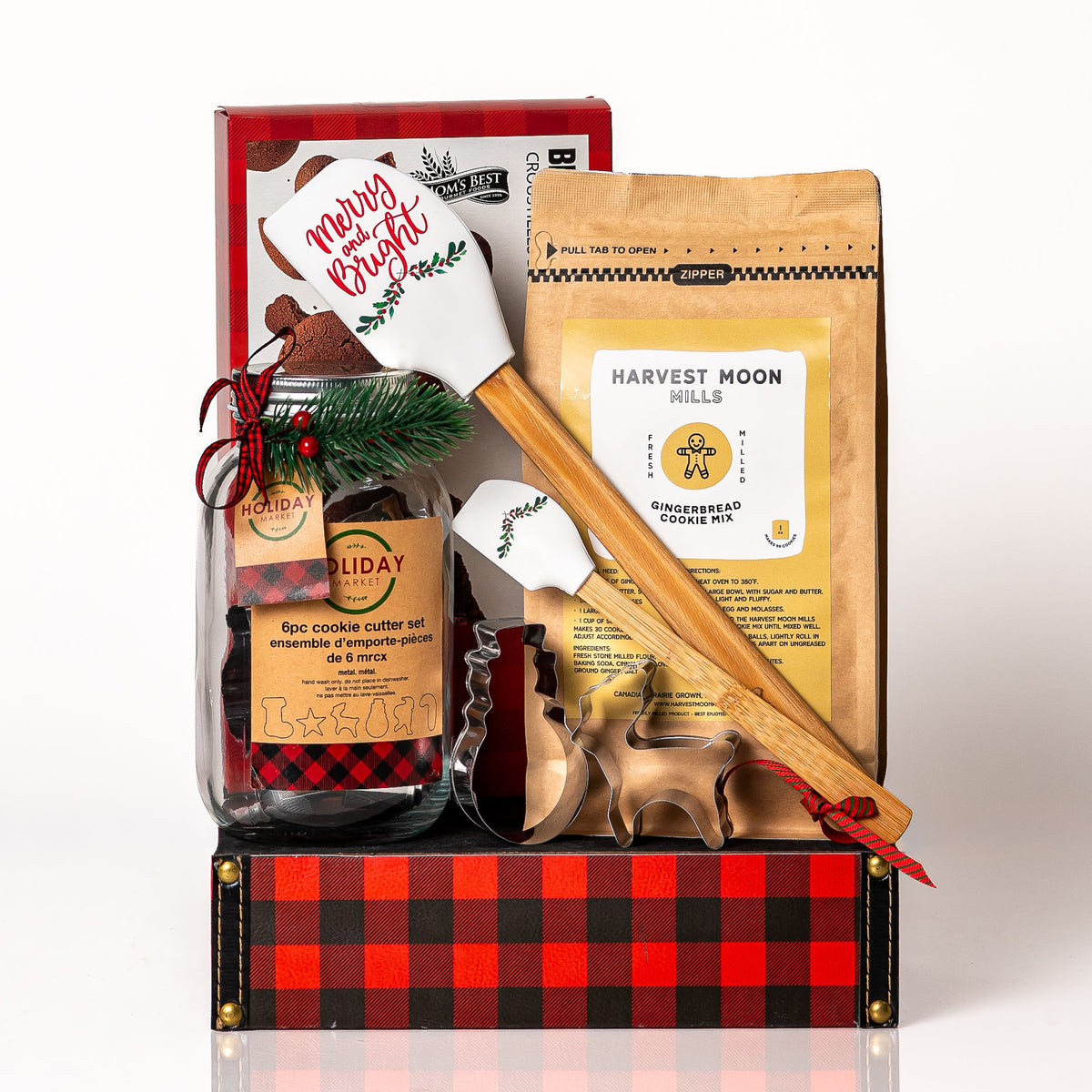 Merry Mixing gift: a red buffalo plaid tray with Harvest Moon Mills gingerbread cookie mix, a holiday spatula set, a jar of cookie cutters and brownie cookie crisps