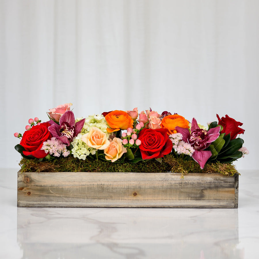 Moonstruck floral arrangement of red roses, orange ranunculus and orchids in a rustic wooden box
