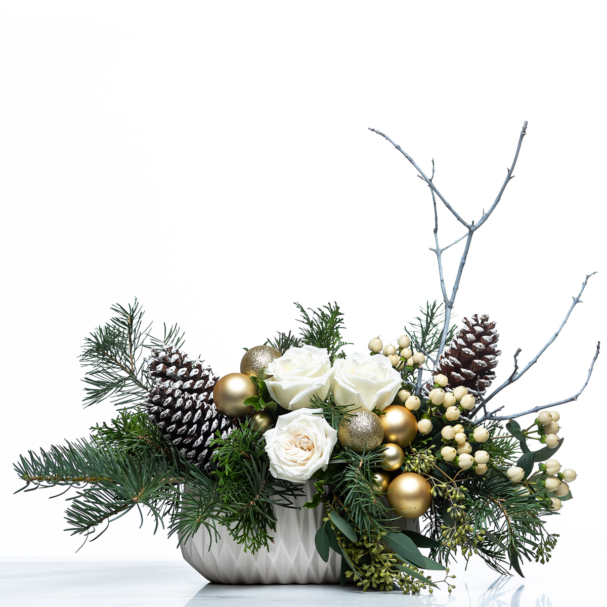 Noel Forest arrangement of white roses, gold baubles, pine cones and evergreen in a white pot
