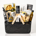 Pantry Provisions: a black metal market basket with wooden handles holding a bottle of Pinot Grigio, egg tagliatelle, My Mother's olive oil, an oil and vinegar bottle, Kanel peppercorns, pesto, tapenade, crackers, pistachios and almond biscotti