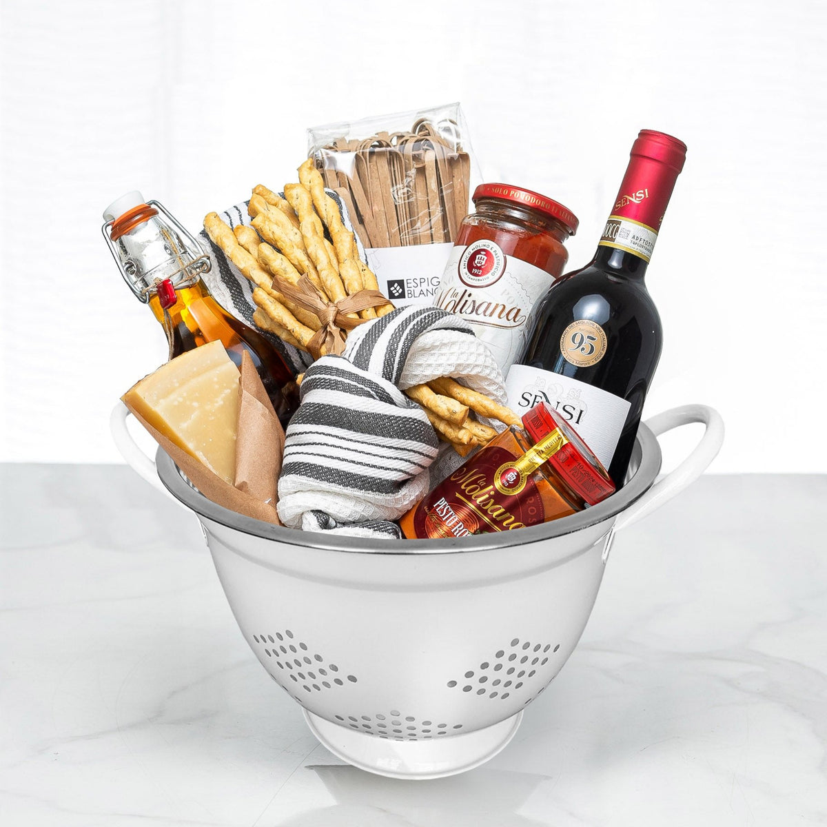 Pasta Pomodoro gift in a white colander with dried pasta, sauces, breadsticks and a striped tea towel