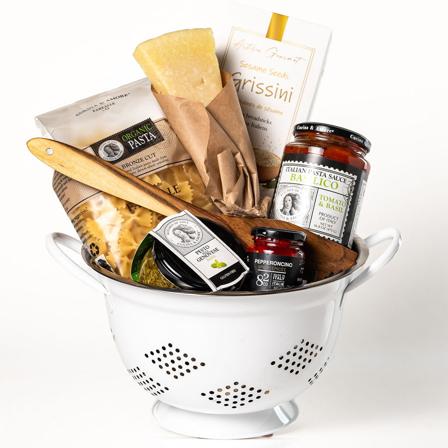 Pasta Pomodoro: a colander filled with Cucina & Amore farfalle, tomato and basil pasta sauce, basil pesto, a Parmigiano wedge, sesame grissini, pepperoncino and a wooden spatula