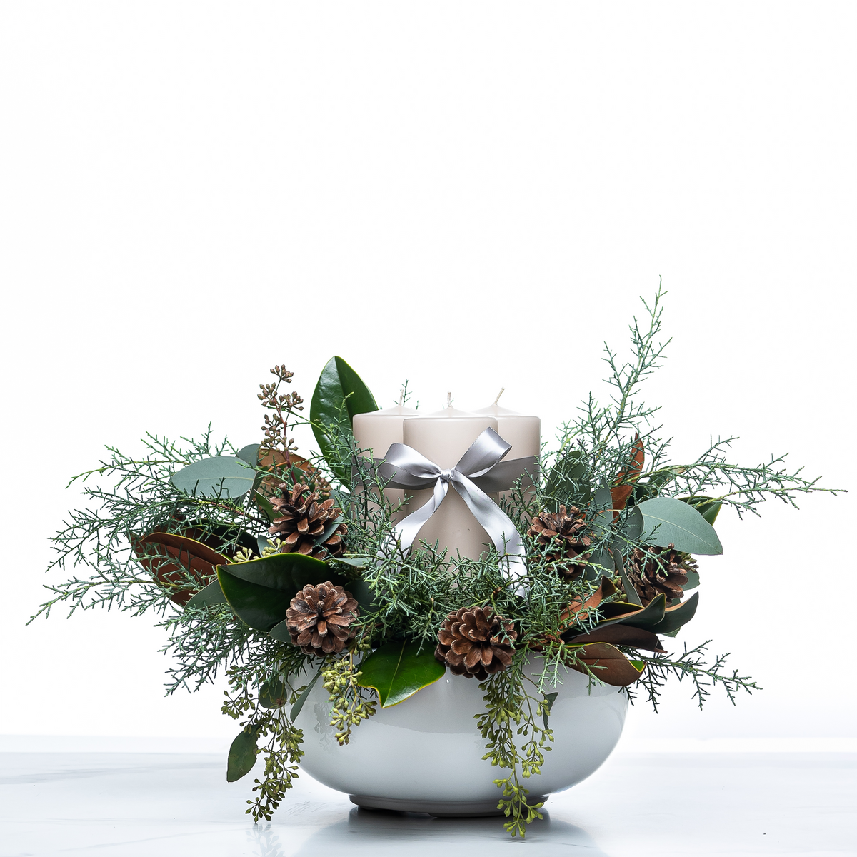 Pillar and Pine holiday centrepiece with a silver ribboned pillar candle, pine cones and magnolia