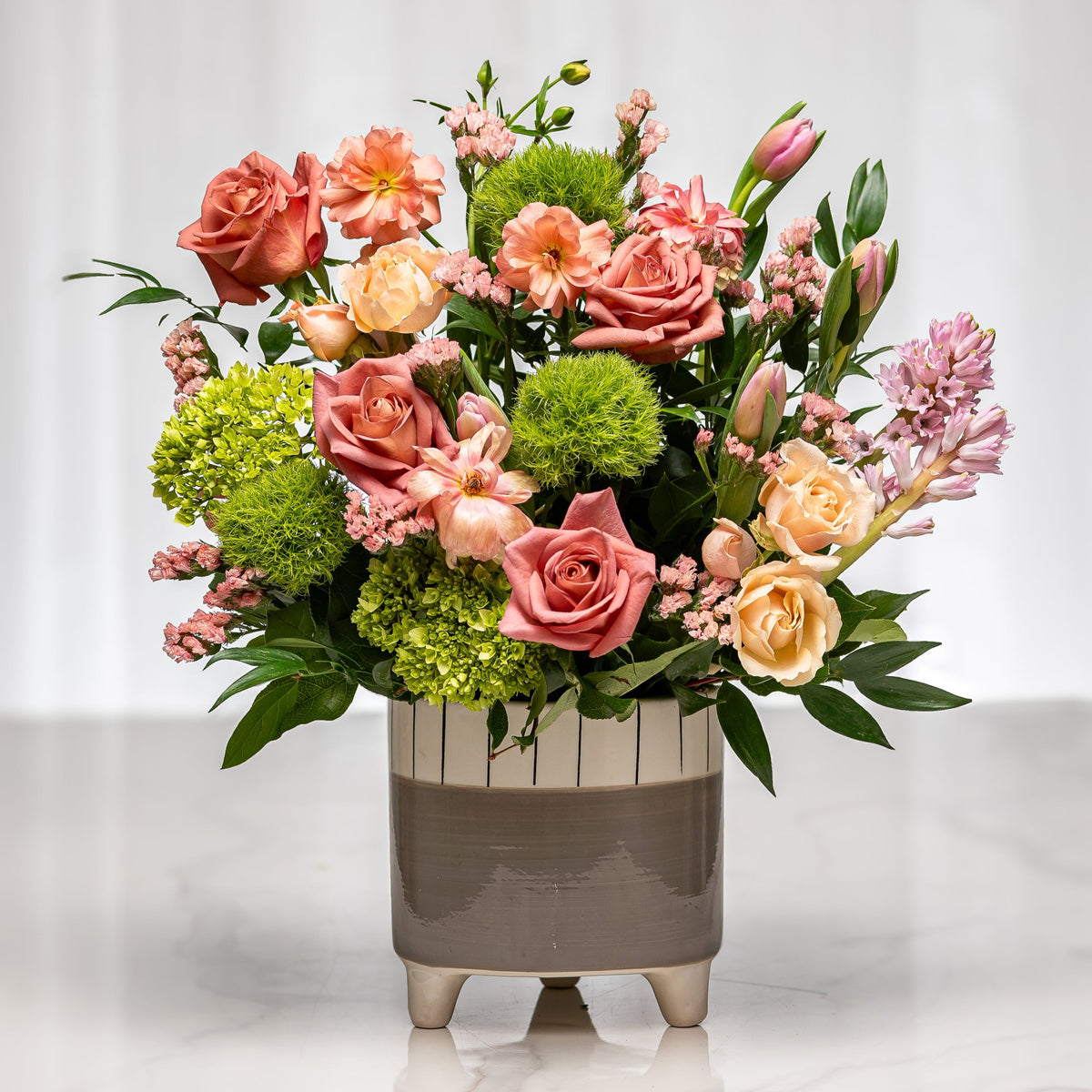 Saffron Skies arrangement of peach roses, green hydrangea and protea in a footed grey pot