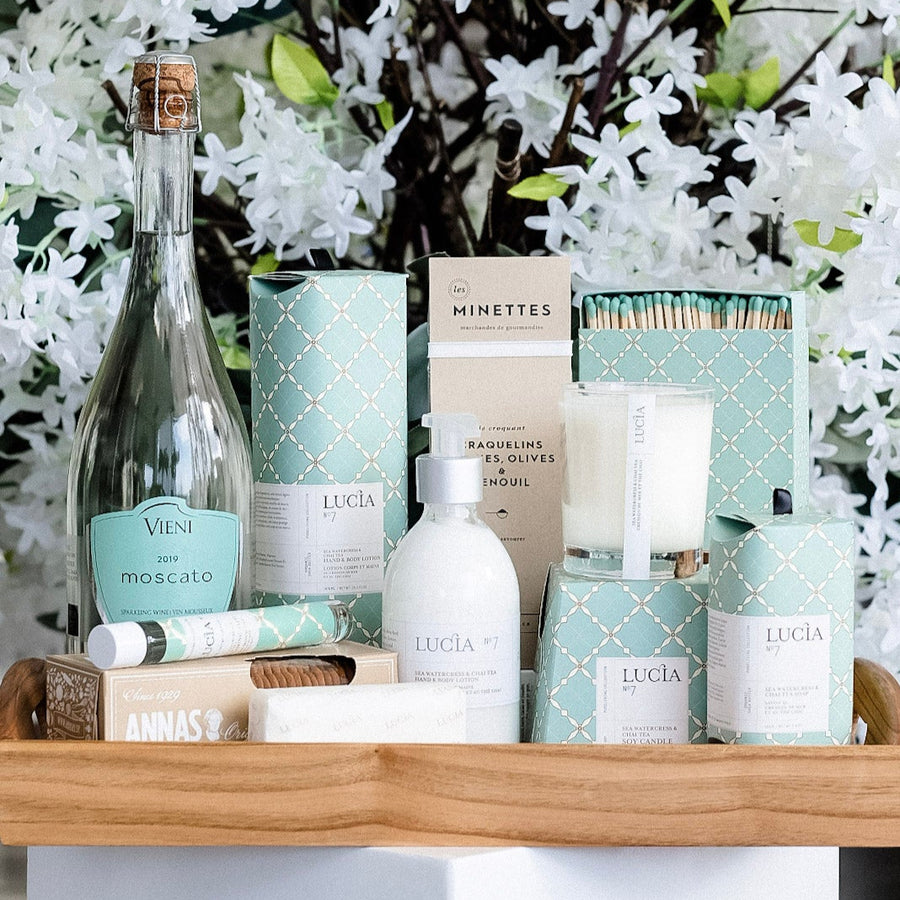 Sea Foam Escape spa gift basket on a wooden tray with Lucia bath and body products, a candle and Vieni Moscato
