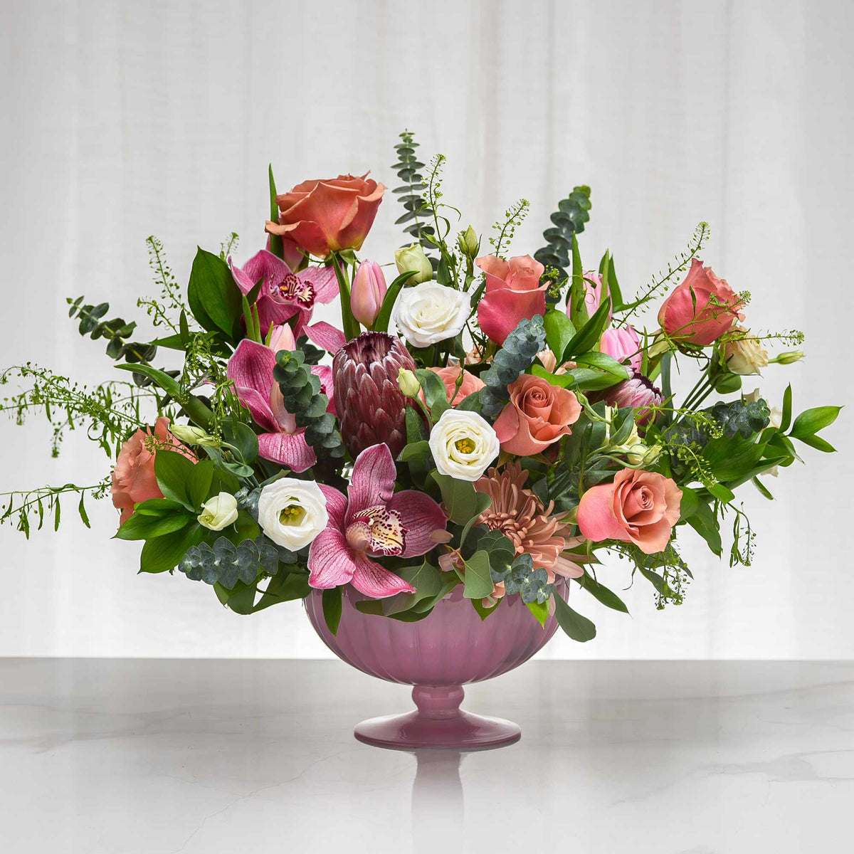 Secret floral arrangement of pink roses, protea and mixed blooms in a lilac footed vase