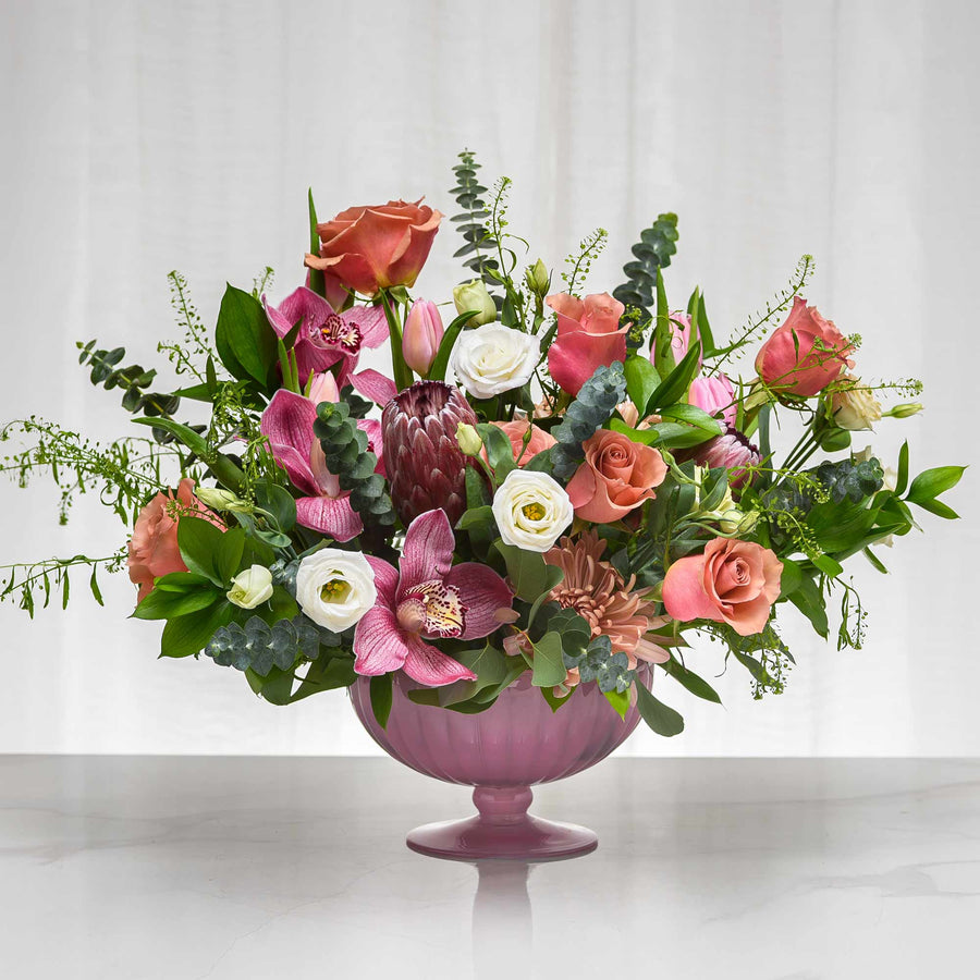 Secret floral arrangement of pink roses, protea and mixed blooms in a lilac footed vase